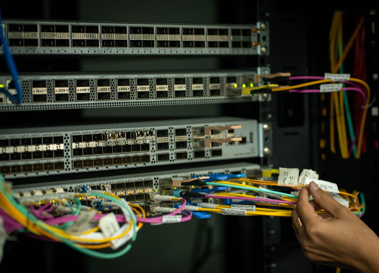 Mão manuseando cordões ópticos identificados por etiqueta em um rack